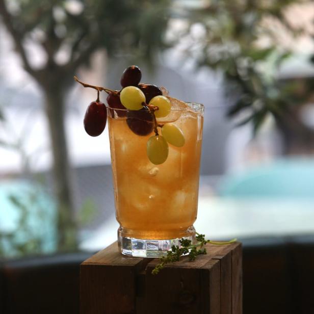 Ein Cocktail mit Eis und Trauben steht auf einer Holzkiste.