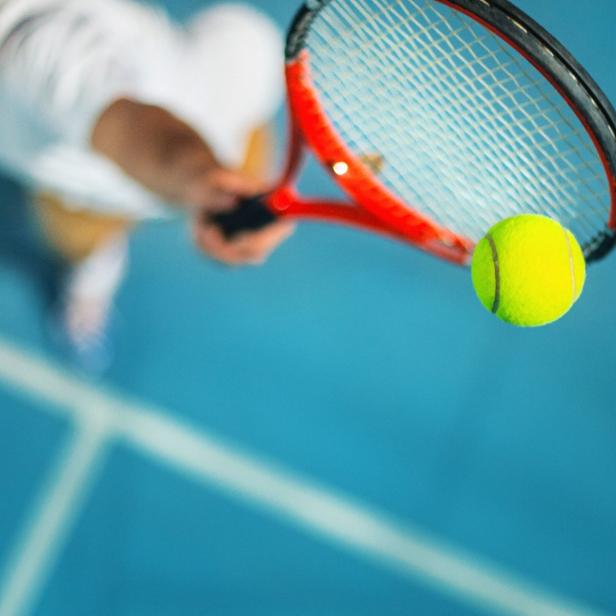 Ein Tennisspieler schlägt einen gelben Ball mit einem roten Schläger.