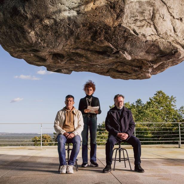 Penélope Cruz, Antonio Banderas und José Luis Gómez sitzen unter einem riesigen Felsen.