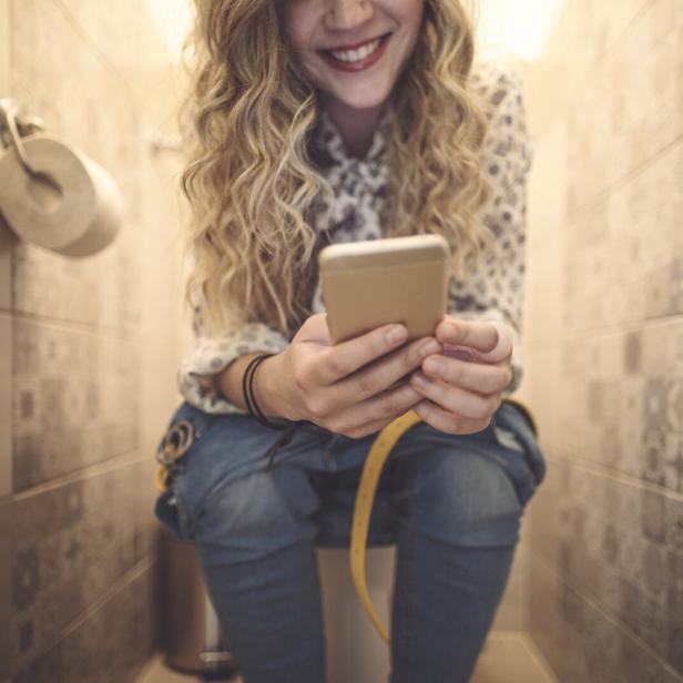 Eine Frau sitzt auf der Toilette und benutzt ihr Smartphone.