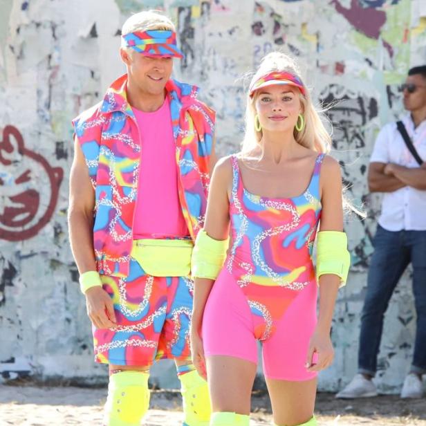 Margot Robbie und Ryan Gosling in farbenfrohen Outfits und Rollschuhen am Set von „Barbie“.