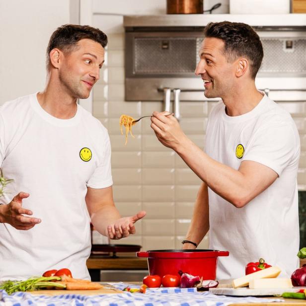 Zwei Männer in T-Shirts mit Smiley-Aufdruck stehen in einer Küche und kochen Pasta.