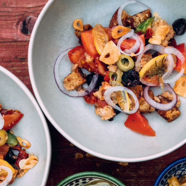 Ein Teller Panzanella-Salat mit Tomaten, Oliven, Zwiebeln und geröstetem Brot.