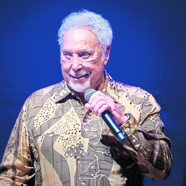 Tom Jones hält ein Mikrofon und lächelt.