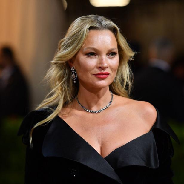 Kate Moss trägt ein schwarzes Kleid und auffälligen Schmuck.