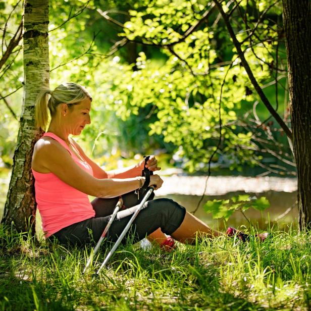 Eine Frau macht eine Pause beim Nordic Walking im Wald.