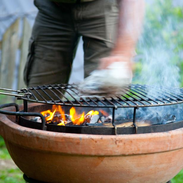 Ein Mann bereitet einen Grill in einem Terrakotta-Topf vor.