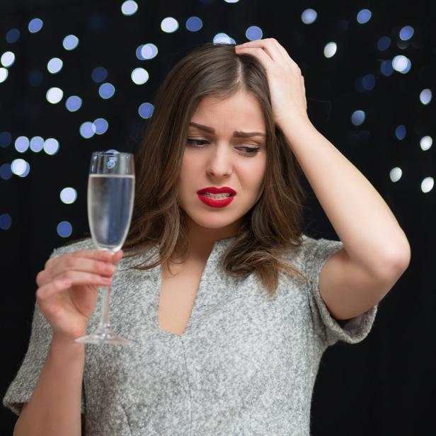 Eine Frau mit rotem Lippenstift blickt besorgt auf ein Glas Sekt.