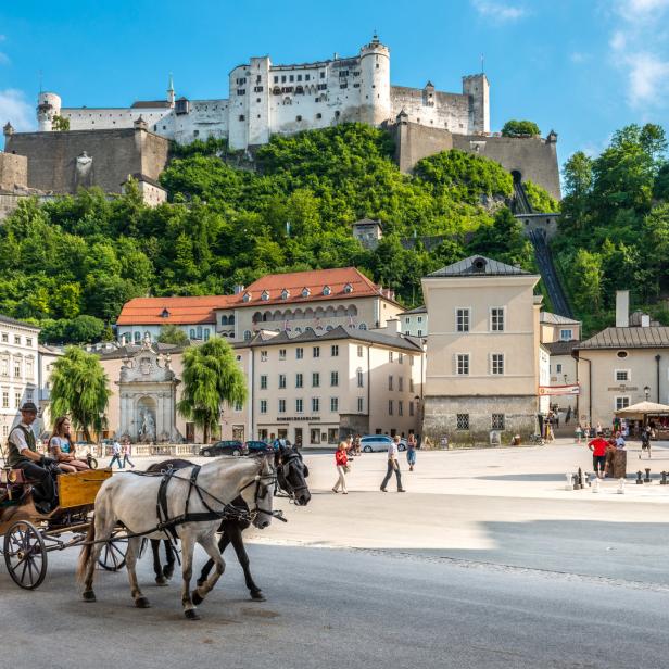 Pferdekutsche fährt über den Residenzplatz in Salzburg mit der Festung Hohensalzburg im Hintergrund.