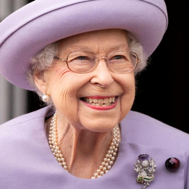 Königin Elisabeth II. lächelt in einem lila Hut und passendem Kostüm.