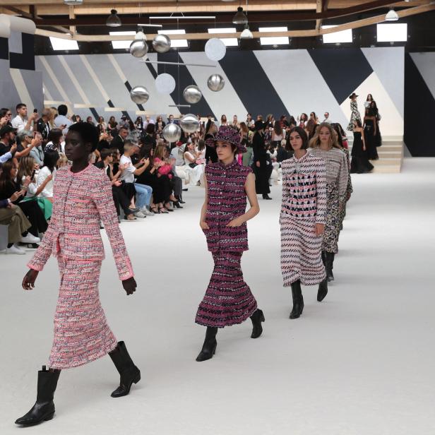 Models präsentieren Tweed-Ensembles auf einem Laufsteg vor Publikum.