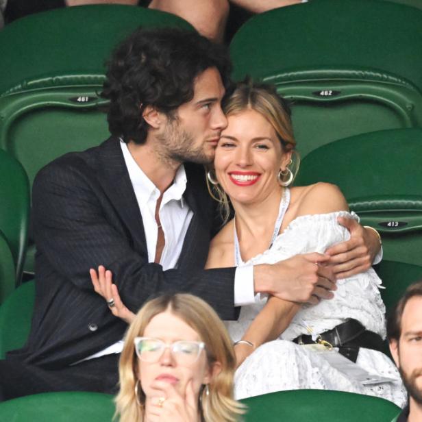 Ein Mann küsst Sienna Miller auf die Wange, während sie auf der Tribüne sitzen.