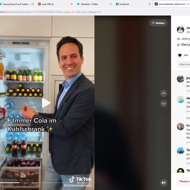 Ein lächelnder Mann in einem Anzug steht vor einem Kühlschrank voller Cola und anderen Getränken.