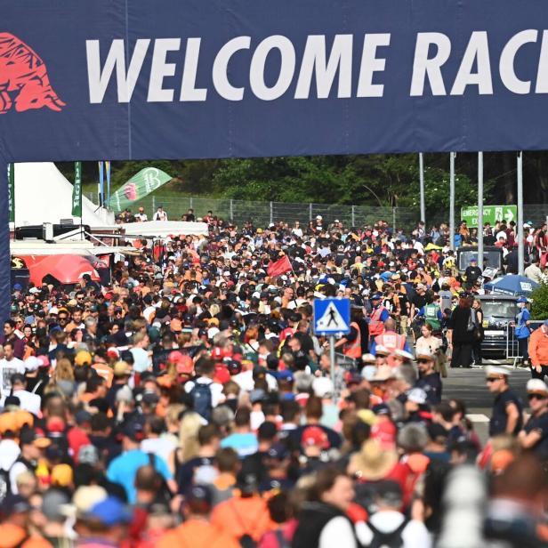 Große Menschenmenge unter einem „WELCOME RACE FANS“-Banner bei einer Motorsportveranstaltung.