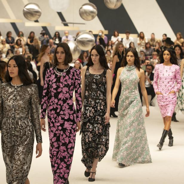 Models präsentieren florale Kleider auf einem Laufsteg vor Publikum.