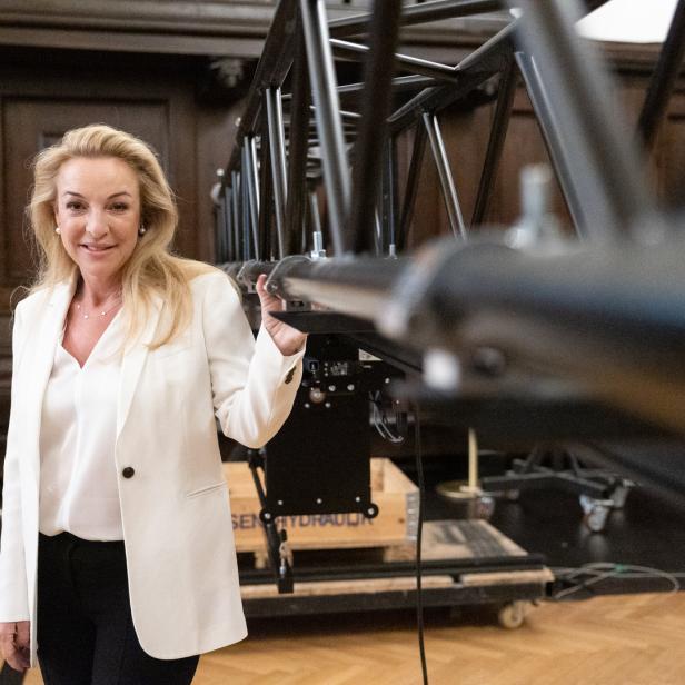 Eine Frau in einem weißen Blazer steht neben einer Bühnenkonstruktion.