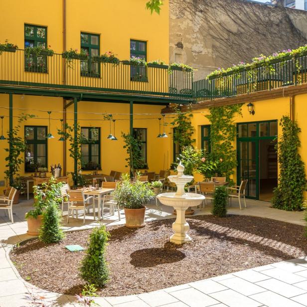 Ein Innenhof mit gelben Wänden, einem Brunnen und Tischen für ein Restaurant.
