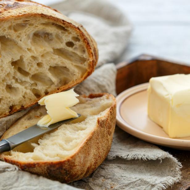 Ein angeschnittenes Brotlaib mit Butter und einem Messer auf einem Küchentuch.