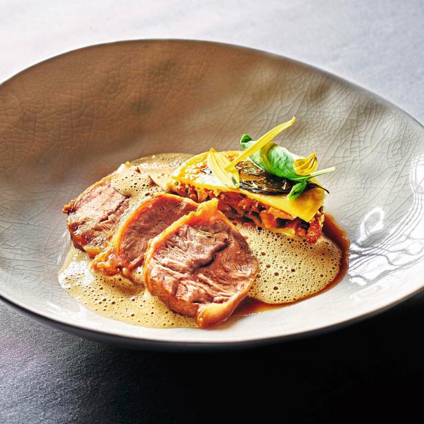 Ein Teller mit drei Scheiben Fleisch, Lasagne und einer hellen Soße.