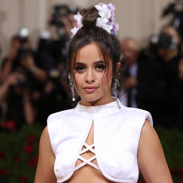 Camila Cabello mit Blumen im Haar und weißem Kleid auf dem roten Teppich.