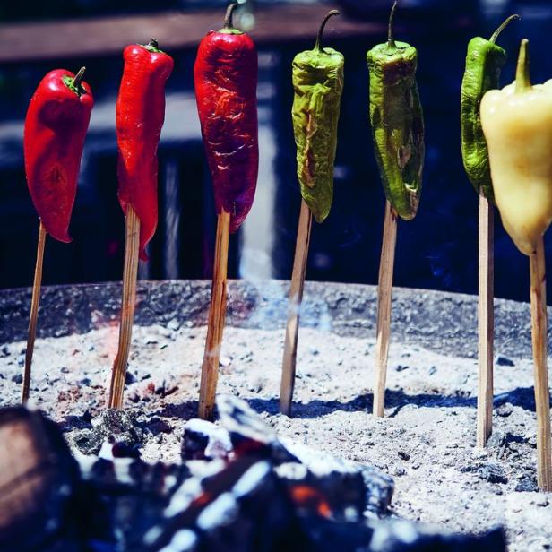 Verschiedene Paprikaschoten auf Spießen werden über glühenden Kohlen gegrillt.