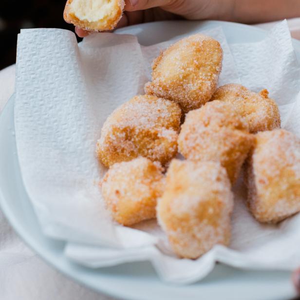 Eine Hand hält einen halbierten, zuckerbestreuten Krapfen über einem Teller mit weiteren Krapfen.