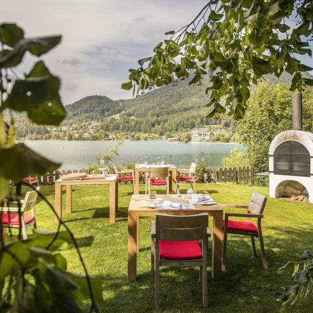 Ein Restaurantgarten mit Tischen und Stühlen am Ufer eines Sees.