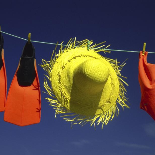 Badebekleidung, Flossen, Sonnenhut und Sonnenbrille hängen an einer Wäscheleine vor blauem Himmel.