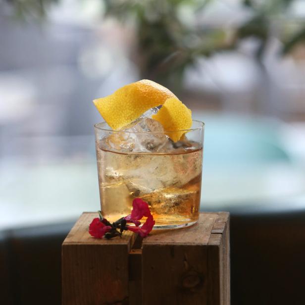 Ein Cocktail mit Eis und Zitronenzeste steht auf einer Holzkiste.