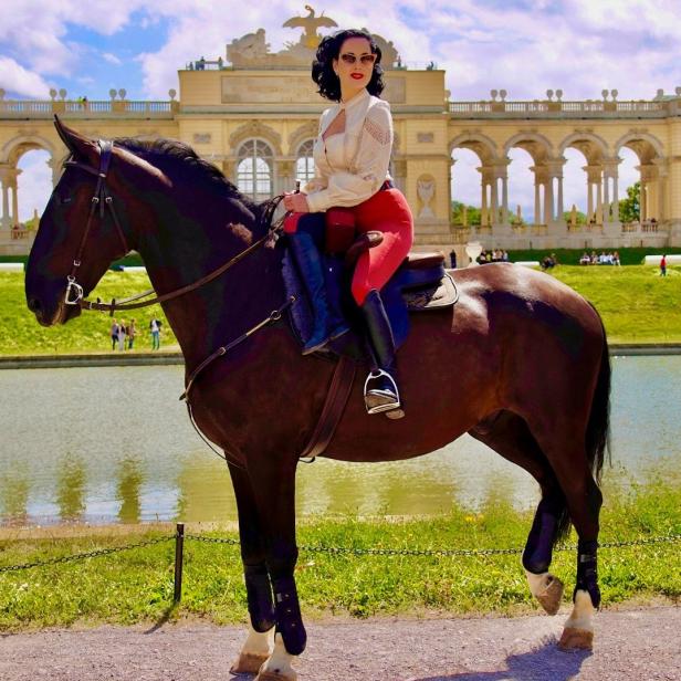 Eine Frau mit roter Hose reitet auf einem Pferd vor dem Schloss Schönbrunn.