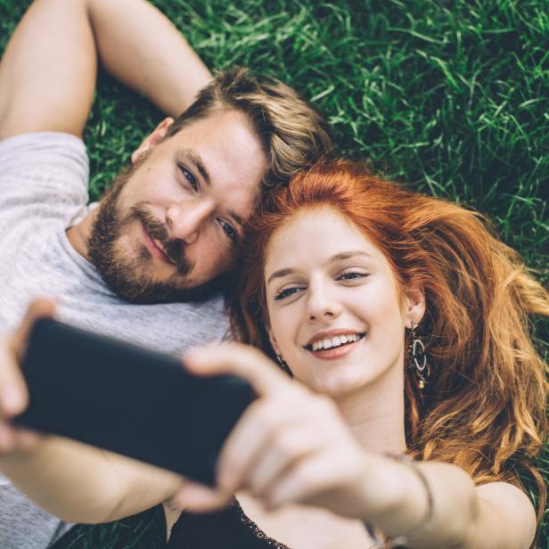 Ein glückliches Paar liegt im Gras und macht ein Selfie.