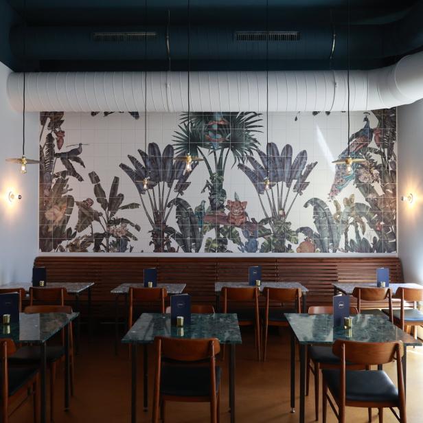 Ein Restaurant mit Tischen und Stühlen vor einer Wand mit Dschungelmotiven.