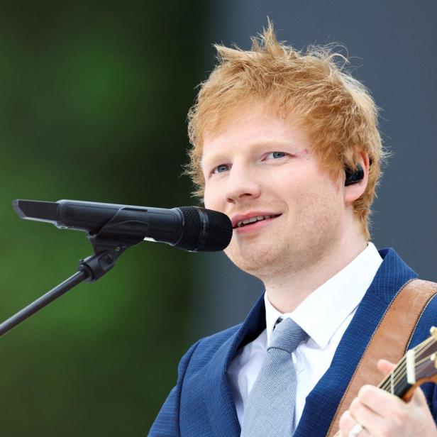 Ed Sheeran singt mit Gitarre in einem blauen Anzug.