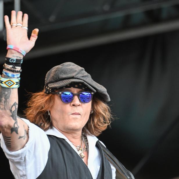 Johnny Depp mit Schirmmütze und Sonnenbrille hebt die Hand.