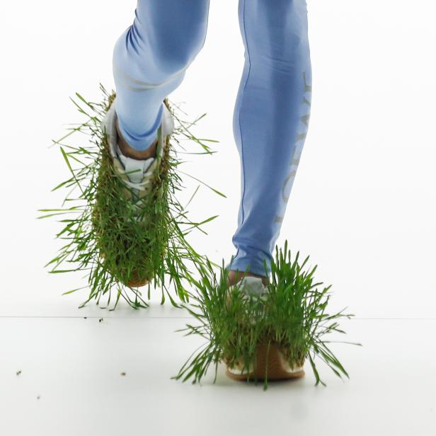 Ein Model präsentiert Schuhe, die mit Gras bewachsen sind, auf dem Laufsteg von Loewe.