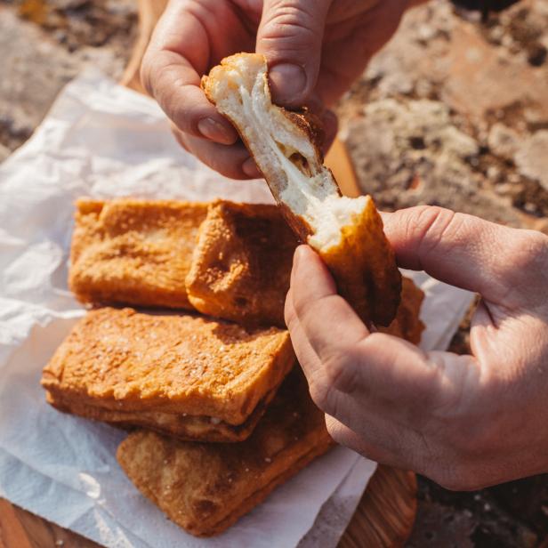 Eine Person teilt ein frittiertes Käsebrot auf einem Holzbrett.