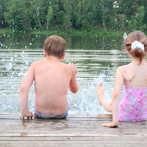 Ein Junge und ein Mädchen sitzen auf einem Holzsteg und lassen ihre Füße ins Wasser baumeln.