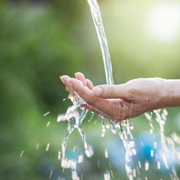 Wasser fließt über die Hand einer Person vor einem grünen Hintergrund.