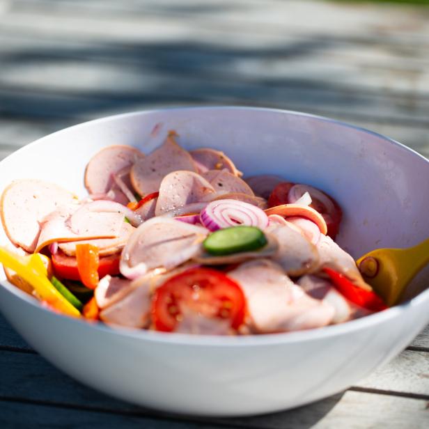 Ein Schüssel Wurstsalat mit Tomaten, Gurken und Zwiebeln auf einem Holztisch.