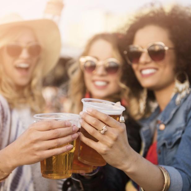 Drei junge Frauen stoßen mit Bier auf einem Festival an.