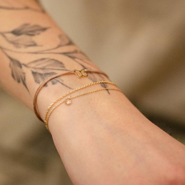 Am Arm einer Frau mit Tattoo befinden sich goldene Armbänder.