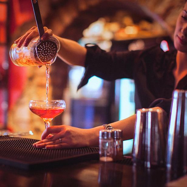 Eine Barkeeperin gießt ein Getränk durch ein Barsieb in ein Cocktailglas.