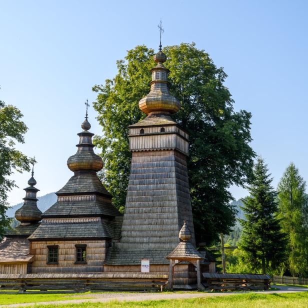 Eine hölzerne Kirche mit mehreren Türmen und Kreuzen inmitten grüner Bäume.