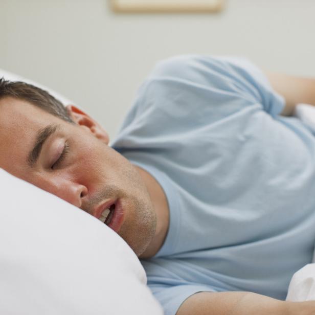 Ein Mann schläft in einem hellen, weißen Bett.