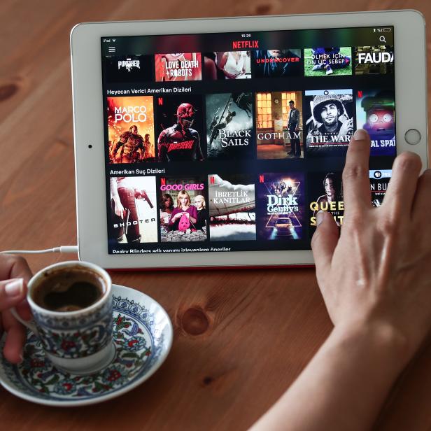 Eine Hand tippt auf einem iPad mit der Netflix-App, daneben eine Tasse türkischer Kaffee.