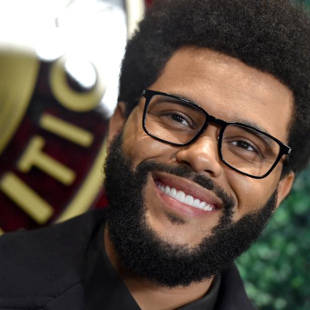 Der lächelnde Sänger The Weeknd mit Brille und Bart vor grünem Hintergrund.