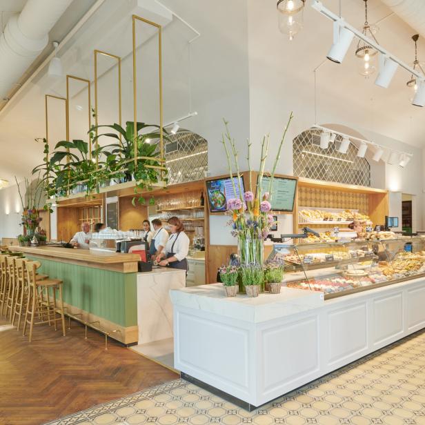 Innenansicht eines hellen Cafés mit Theke, Auslagen und Sitzbereich.