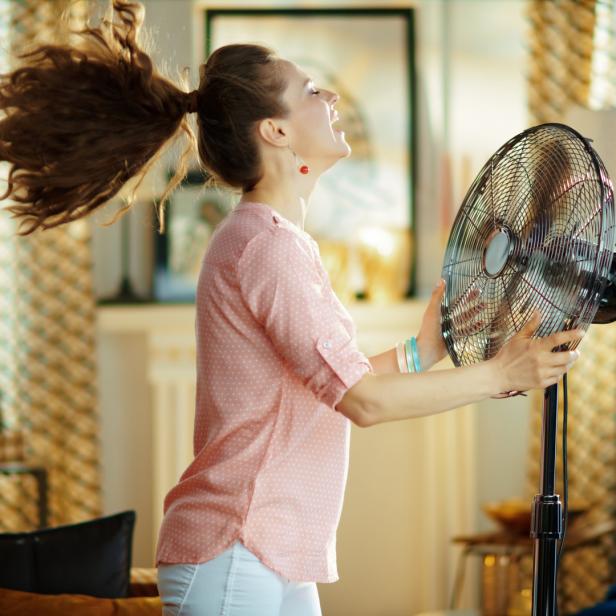 Eine Frau genießt die Kühle eines Ventilators in einem Wohnzimmer.