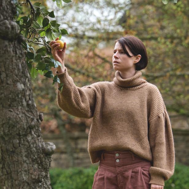 Eine Frau in einem Garten pflückt eine gelbe Frucht von einem Baum.