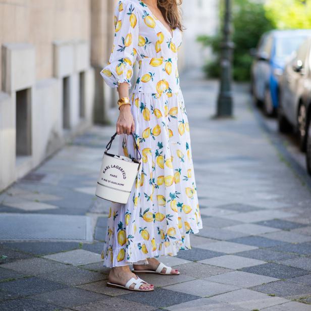 Eine Frau in einem langen, weißen Kleid mit Zitronenmuster und einer Karl Lagerfeld Handtasche.